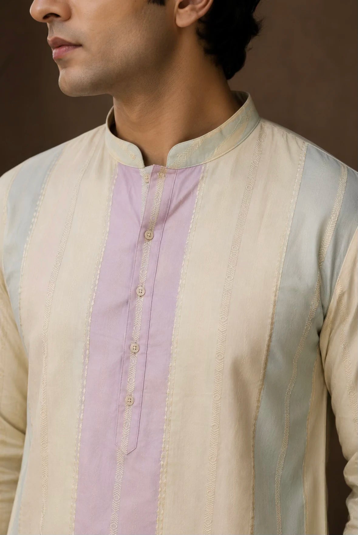 A close-up of a man wearing a cream-colored kurta with a vertical lavender panel down the front, featuring gold embroidery and a mandarin collar.