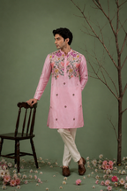 Man wearing pink floral embroidered kurta standing near a chair