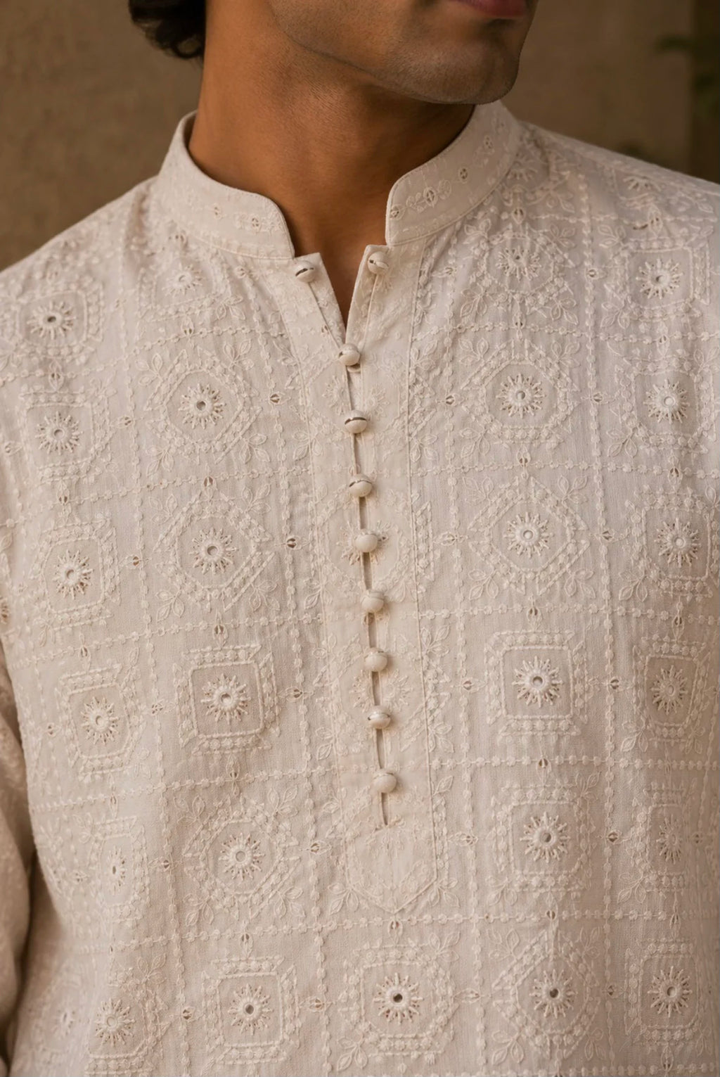 Close-up of a man wearing a cream-colored embroidered kurta with a mandarin collar and decorative button placket.